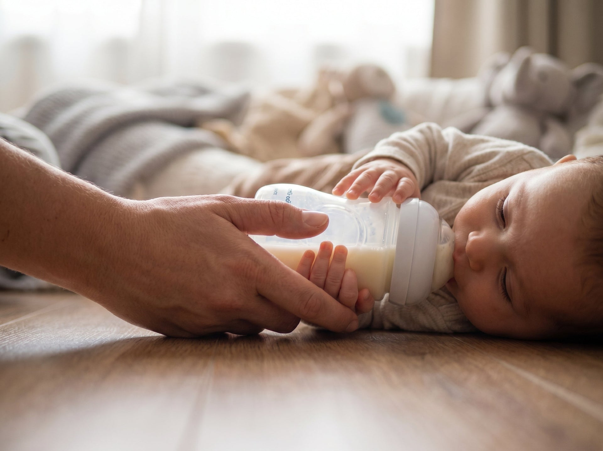 Close-up photograph of practicing paced bottle feeding with an ergonomic glass anti-colic baby bottle held parallel to the floor to prevent flow shock and gas.